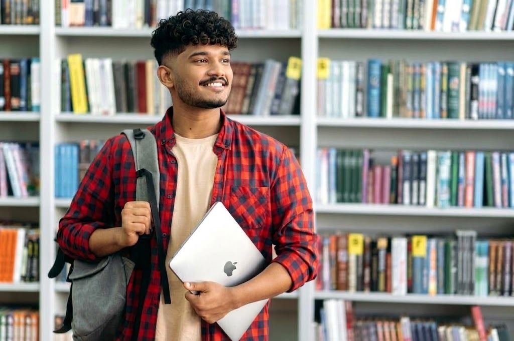 Smiling student with a laptop and backpack in a library